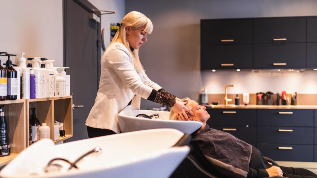 Kund får en avkopplande hårtvätt av en uppmärksam frisör på Team Linda Falck, en frisörsalong i Göteborg, omgiven av stilrena och moderna inredningsdetaljer samt en hylla full av professionella hårvårdsprodukter.