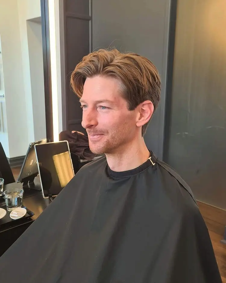 Nöjd kund i frisörstolen med en trendig herrklippning och mittbena, skapad med klassiskt saxarbete hos Team Linda Falck.